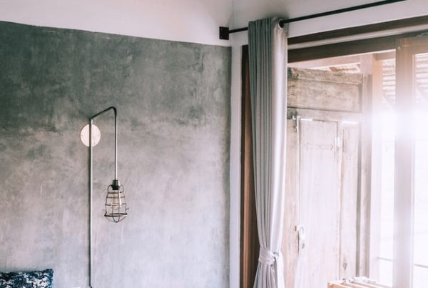 A grey, concrete bedroom, with a white bed and large window