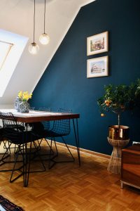 Dining room, with dark blue painted wall, a dark table with black metal chairs and a brown vinyl flooring