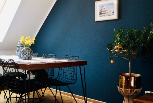 Dining room, with dark blue painted wall, a dark table with black metal chairs and a brown vinyl flooring