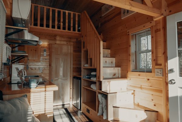 A small wooden house, with wooden stairs leading to a cosy living room and kitchen