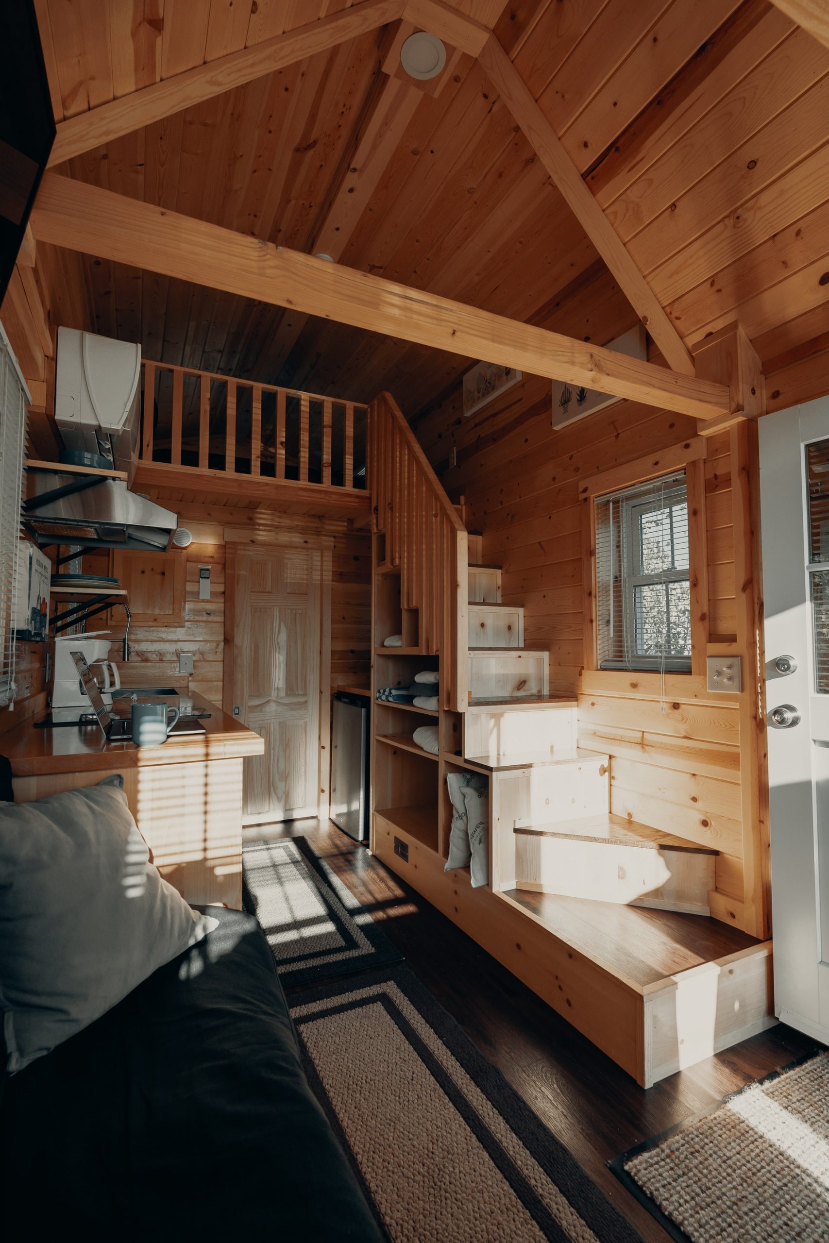 A small wooden house, with wooden stairs leading to a cosy living room and kitchen