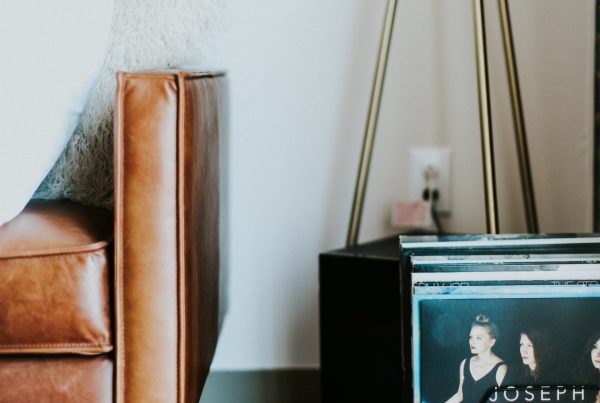 brown cushioned chair, against a white wall, with black vinyl records sat on a wooden vinyl floor